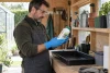 Un jardinier protégé lit l’étiquette floutée d’un produit phytosanitaire fermé